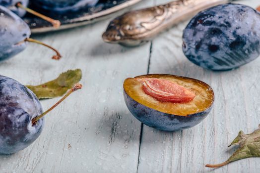 Ripe plums with sliced fruits, leaves and vintage knife over light wooden surface