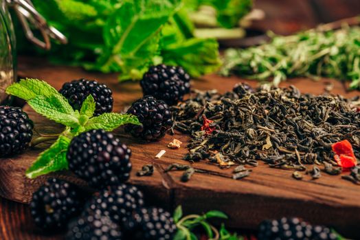 Heap of Dry Green Tea and Fresh Blackberries on Wooden Cutting Board. Bundles of Mint and Thyme Leaves.