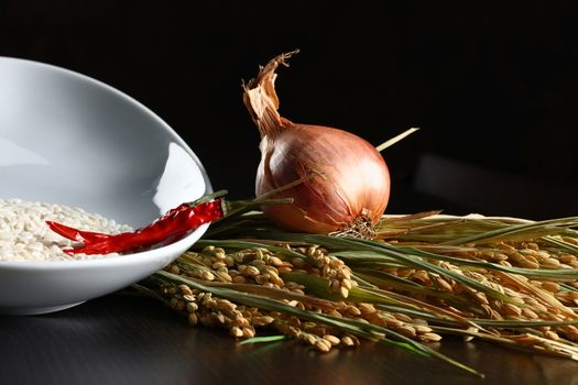 Close up of onions, rice and chilli. Healthy organic raw food ready for cooking on a dark wood table top.