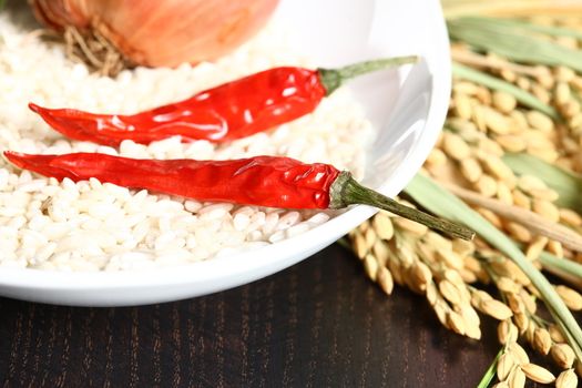 Extreme close up of hot chilli and rice corns in a white bowl with rice plants in background on a wooden table