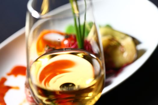 a good meal with wine. Close up of out of focus wine glass with dish in the background showing through the glass