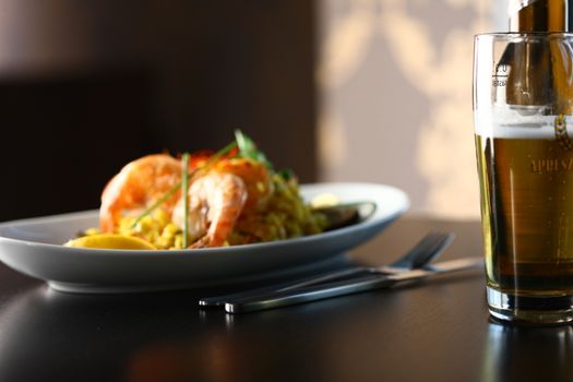 dish with shrimp and salad and a glass of beer in foreground