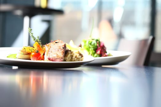 a good meal with meat and salad on white plates with restaurant setting. Table and window in the background