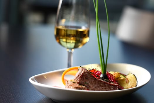 A good meal with wine. Meat, a glass of wine with green leafs on gray table top