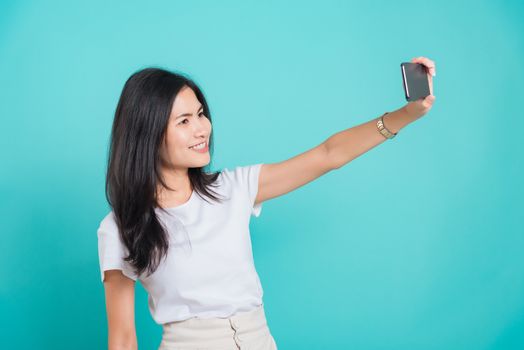 Portrait Asian beautiful happy young woman standing smile, holding mobile phone her taking selfie on blue background, with copy space