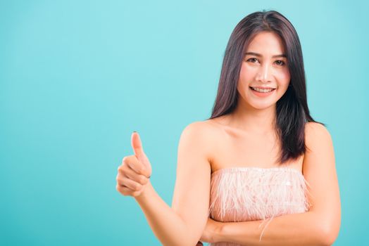 Portrait asian beautiful woman smiling her showing thumbs up and looking to camera on blue background, with copy space for text