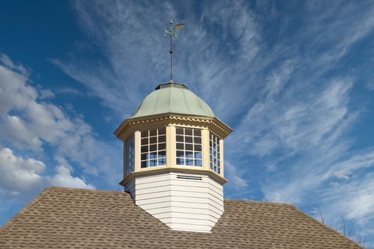 Roof line of a building with wood and copper cupola and weather vane against a clear blue sky