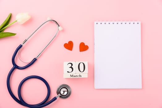 Doctor's Day concept, flat lay top view, equipment medical red heart stethoscope and note book on pink background, care patient in hospital with copy space for text