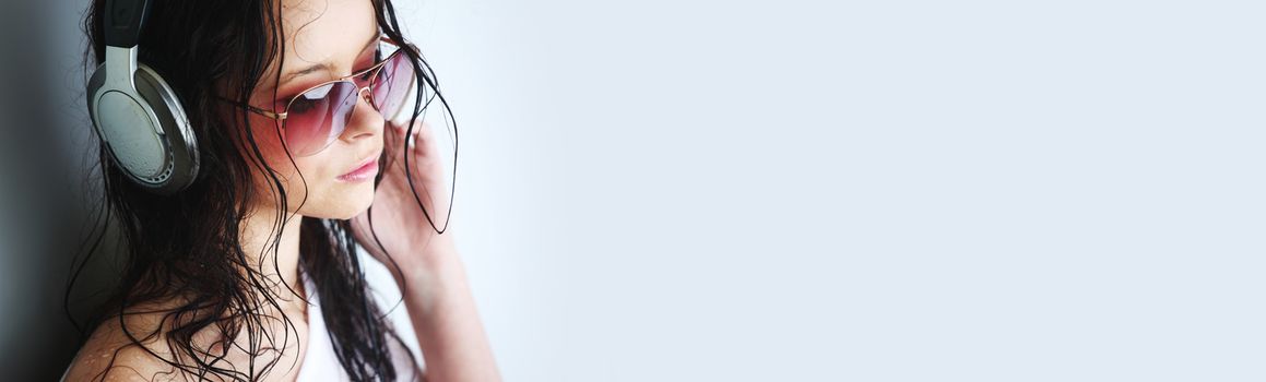 Young woman listening to music on headphones enjoying a dance. Closeup portrait of girl on light background with copy space