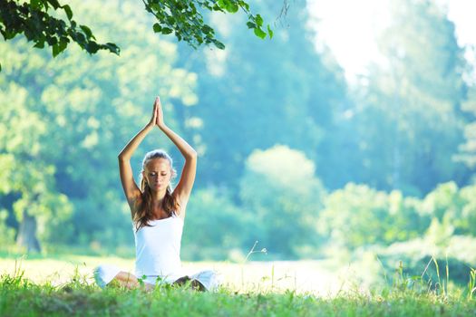 Yoga woman in white on green park grass in lotus asana pose
