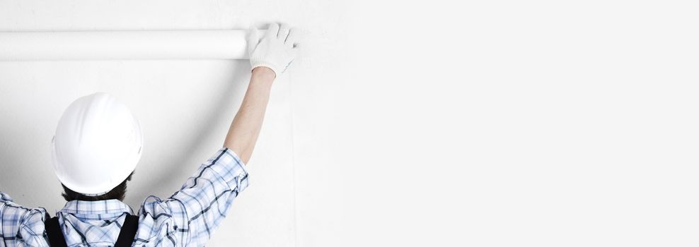 Worker attaching white wallpaper to empty wall copy space on background for text