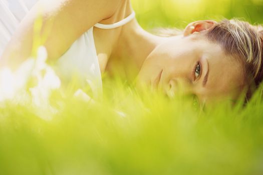 Young attractive blond woman is relaxing in the park laying in grass