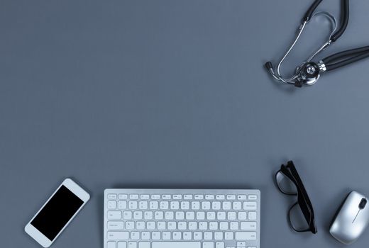 Health care concept in a flat lay consisting of doctor medical equipment gray table with stethoscope, computer keyboard, cell phone and reading glasses.  Top view with copy space. 