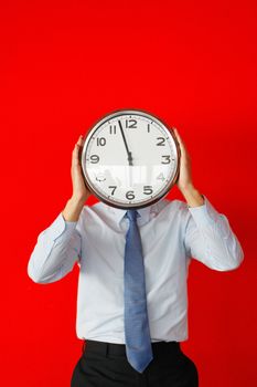 Businessman covering his face with wall clock on red background