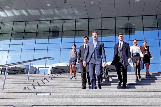 Group of business people and their leader walking down stairs outside office building successul deal negotiation concept