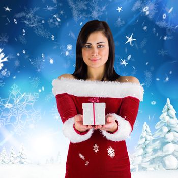 Pretty girl in santa outfit holding gift against snowy landscape with fir trees