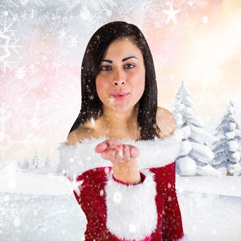 Pretty girl in santa outfit blowing against snowy landscape with fir trees