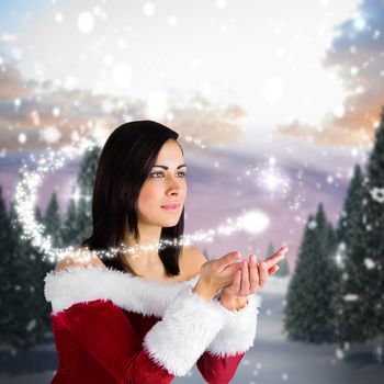 Pretty girl in santa outfit with hands out against snowy landscape with fir trees
