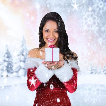 Pretty girl in santa outfit holding gift against snowy landscape with fir trees