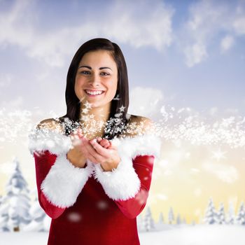 Pretty girl in santa outfit with hands out against snowy landscape with fir trees