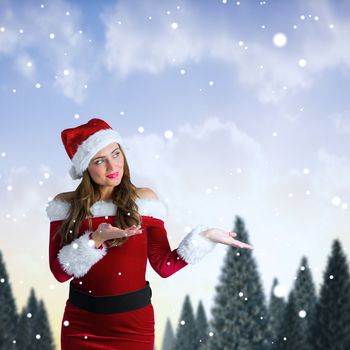 Pretty girl in santa costume holding hand out against snowy landscape with fir trees