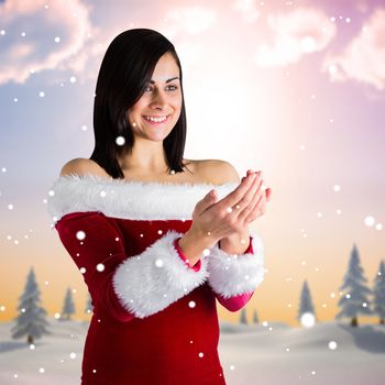 Pretty girl in santa outfit with hands out against snowy landscape with fir trees