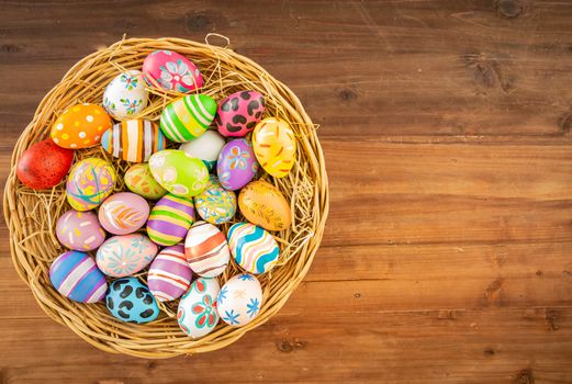 Easter eggs in various patterns and colors in a bird's nest placed on a wooden floor decorated in retro style.