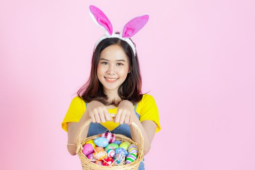 Portrait of a happy young woman wearing Easter bunny ears prepares to celebrate Easter on a pink background.