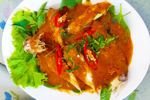 Thailand fried fish in spicy curry sauce on white dish.