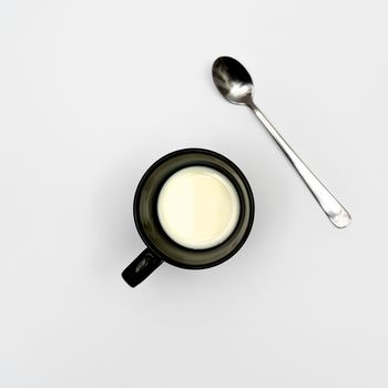 A cup of milk and a tea spoon on a white surface