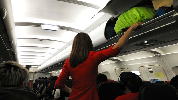 Stewardess helping passenger to loading luggage into overhead bin