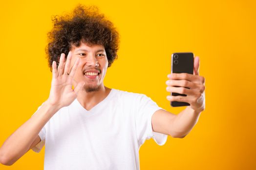 Portrait asian handsome man curly hair taking selfie with mobile phone isolated on yellow background