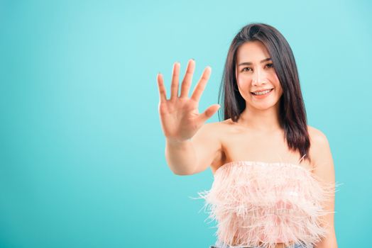 Smiling face Asian beautiful woman showing hand stop sign on blue background, with copy space for text