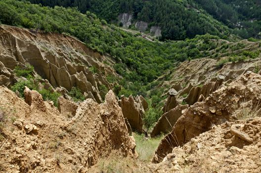 Fragment of the famous Stob Pyramids with unusual shape red and yellow rock formations, green bushes and trees around, west share of Rila mountain, Kyustendil region, Bulgaria, Europe
