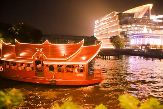 Night photo of Bangkok and a travel boat sailing in a river. Evening life in a big city