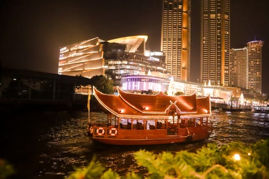 Night photo of Bangkok and a travel boat sailing in a river. Evening life in a big city