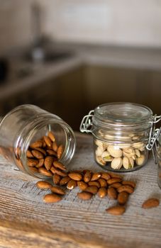 Almonds scattered on the white vintage table from a jar and with other nuts on background. Almond is a healthy vegetarian protein nutritious food. Almonds on rustic old wood