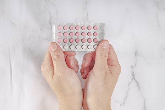 Female hands holding birth control pills on a marble background