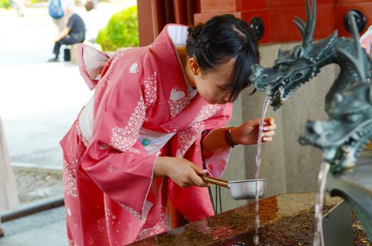 TOKYO, JAPAN - MAY 28, 2018: Young girl wearing Japanese kimono drinking water from a Chozuya as part of a ceremonial purification ritual before entering the Sensoji  Buddhist temple. 