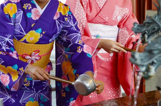 Young girsl wearing Japanese kimono drinking water from a Chozuya as part of a ceremonial purification ritual before entering the Sensoji  Buddhist temple. 