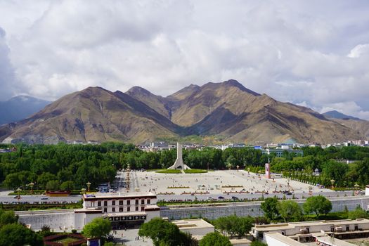 The panoramic view of Lhasa city, in front of Potala Palace and Palace square, with modern building and mountains, far away a Tibet Peaceful Liberation Monument and blue sky