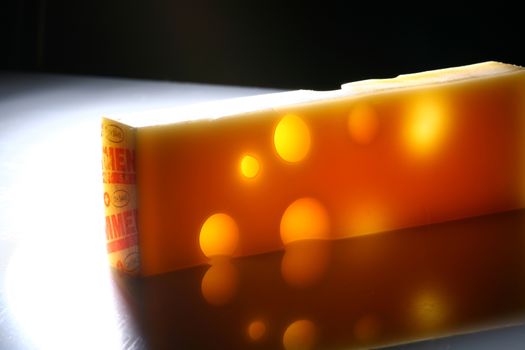 Swiss cheese with holes on table with reflection. Lit from the back