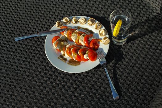 Mozzarella salad with water served outdoors on lounge chair with water and lemon slice