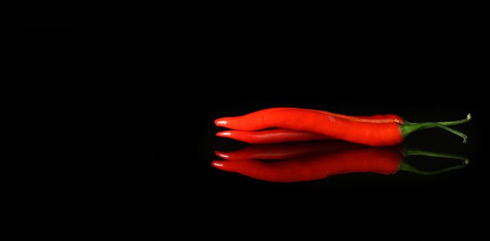 black background with red hot pepper and reflection. Close up of hot chilli