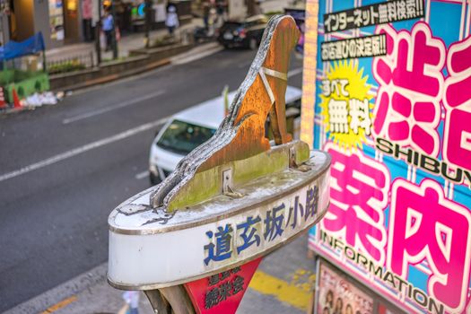 Small lane whose entrance is signaled by a lamppost overcomes a dog silhouette with many grooming salons for dogs and cats adjacent to the dogenzaka street leading to the Shibuya Crossing Intersection in front of Shibuya Station on a bright day blue sky .