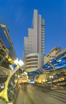 Futuristic architecture with mirroring and transparent blue plastic panels swiveling in Shibuya district in Dogenzaka street leading to Shibuya Crossing Intersection in front of Shibuya Station in a summer evening.