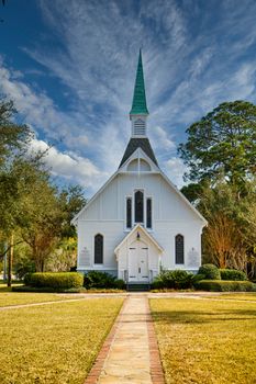 A small white, wooden church down sidewalk under nice sky