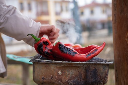 Hand checking red chili peppers grilling on BBQ