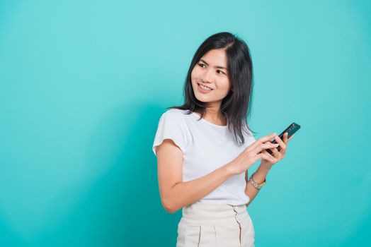 Portrait Asian beautiful happy young woman standing smile, holding mobile phone her looking back to space on blue background, with copyspace