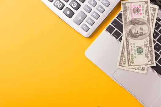 April of the year is Tax Day, Top view flat lay closeup calculator, laptop computer and Dollar money, on yellow background business finance budget concept with copy space for text